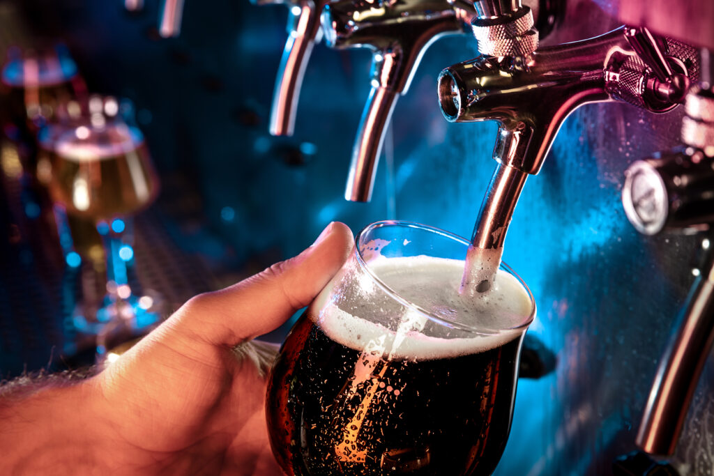 Hand of bartender pouring a large ale, porter, stout beer in tap. Bright and modern neon light, males hands. Pouring beer for client. Side view of young bartender pouring beer while standing at the bar counter.